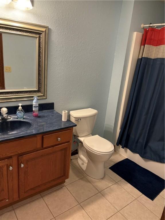 bathroom with toilet, a textured wall, tile patterned flooring, and vanity