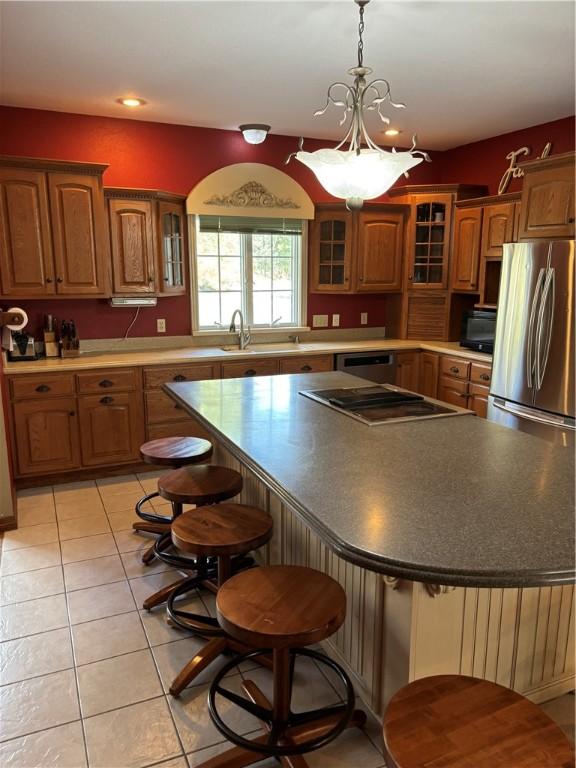kitchen with a center island, brown cabinets, a sink, light tile patterned floors, and a breakfast bar