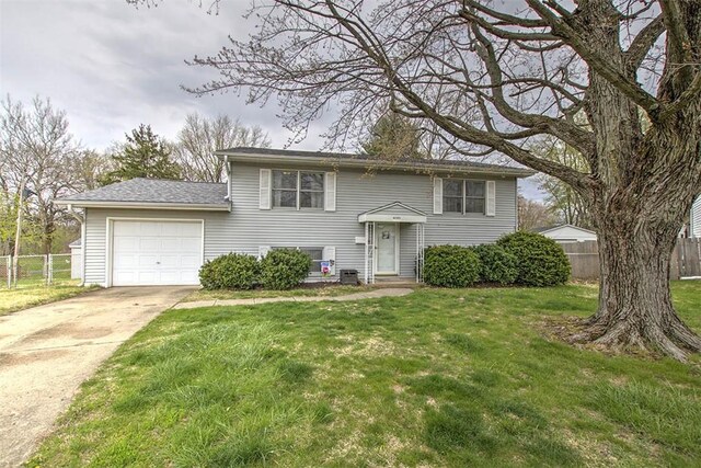 split foyer home featuring driveway, an attached garage, fence, a front yard, and roof with shingles