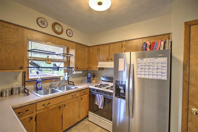 kitchen with under cabinet range hood, light countertops, a sink, gas range gas stove, and stainless steel fridge