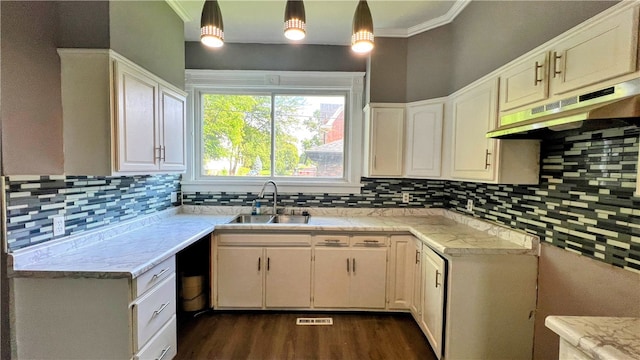 kitchen featuring white cabinetry, sink, hanging light fixtures, backsplash, and ornamental molding