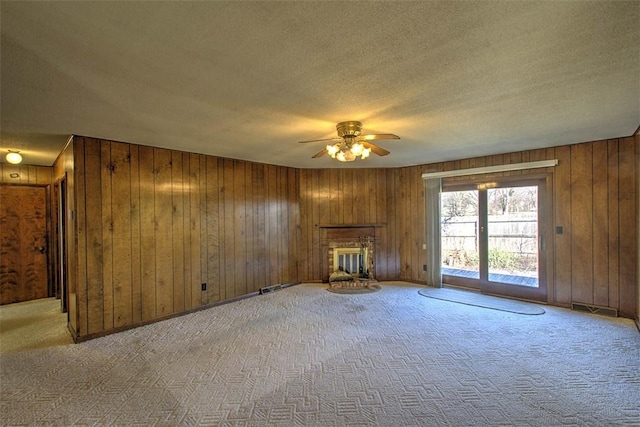 unfurnished living room featuring a fireplace, ceiling fan, wood walls, a textured ceiling, and carpet flooring