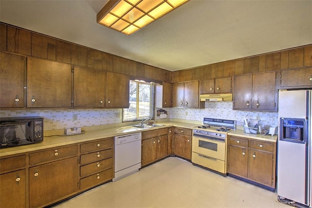 kitchen featuring backsplash, under cabinet range hood, light countertops, white appliances, and a sink