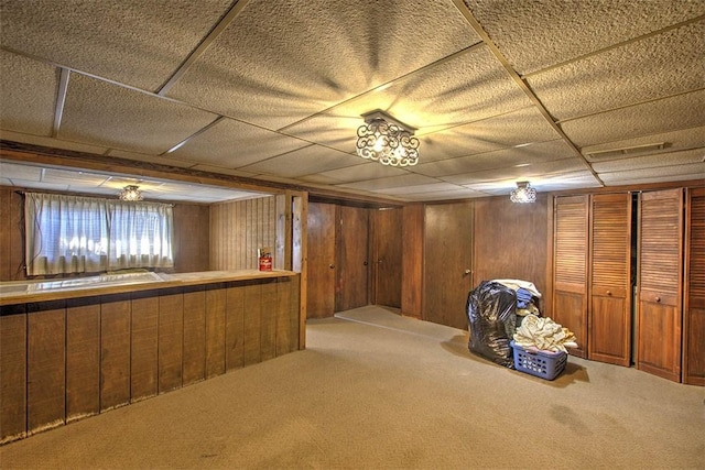 basement with a paneled ceiling, wooden walls, and carpet flooring