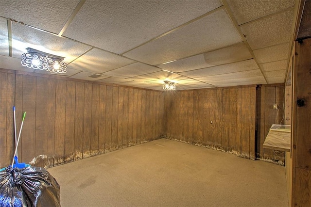 finished below grade area with a paneled ceiling, carpet, and wood walls