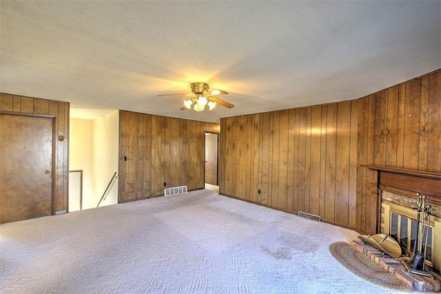 unfurnished living room featuring visible vents, wood walls, carpet floors, and a glass covered fireplace