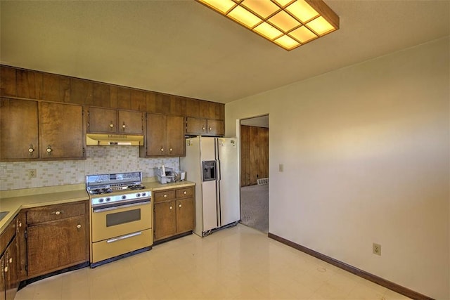 kitchen with under cabinet range hood, tasteful backsplash, gas stove, white fridge with ice dispenser, and light countertops