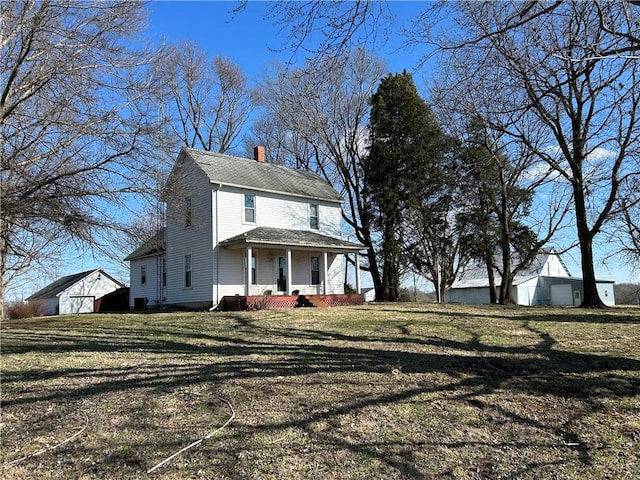 view of front of house with covered porch, a chimney, a front yard, and an outbuilding