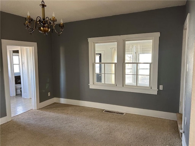 carpeted empty room with a notable chandelier, baseboards, and visible vents