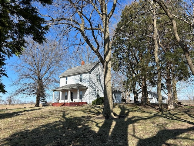 view of front of house featuring covered porch, a front yard, roof with shingles, and a chimney