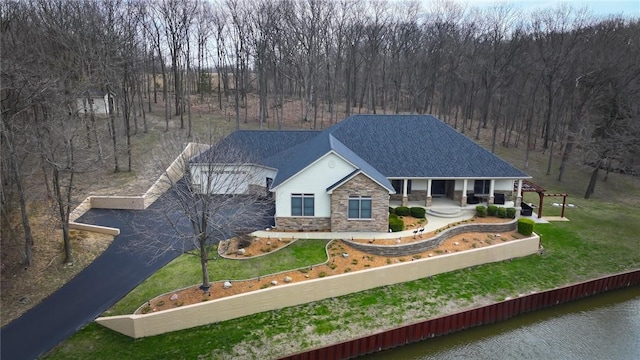 view of front of house featuring stone siding, a water view, a front yard, driveway, and a shingled roof