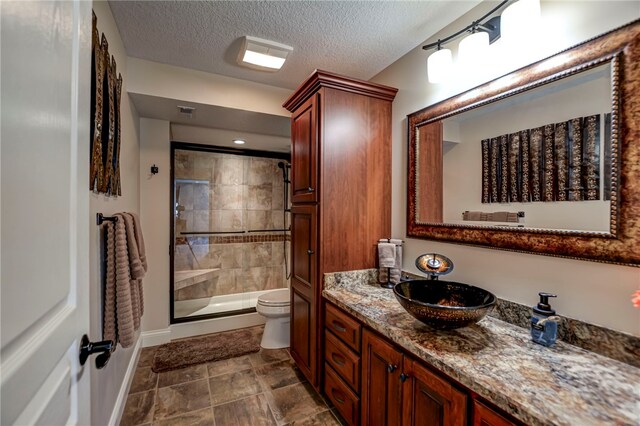 full bath featuring vanity, a tile shower, toilet, baseboards, and a textured ceiling