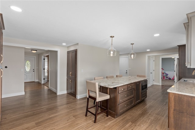 kitchen with light stone countertops, a center island, hanging light fixtures, and dark wood-type flooring