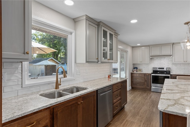 kitchen with hanging light fixtures, sink, light wood-type flooring, appliances with stainless steel finishes, and tasteful backsplash