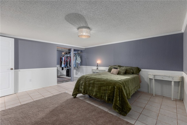 bedroom featuring a walk in closet, ornamental molding, a textured ceiling, light tile patterned floors, and a closet