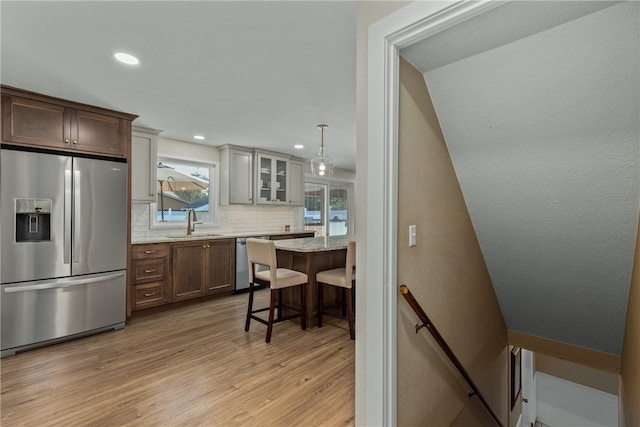 kitchen featuring appliances with stainless steel finishes, light wood-type flooring, backsplash, sink, and a breakfast bar area