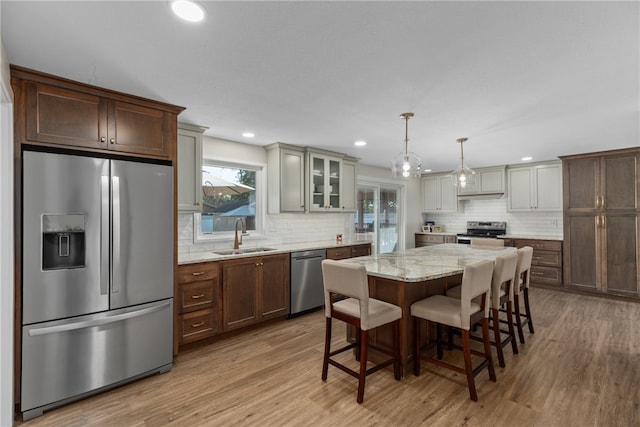 kitchen featuring stainless steel appliances, sink, pendant lighting, light hardwood / wood-style floors, and a kitchen island