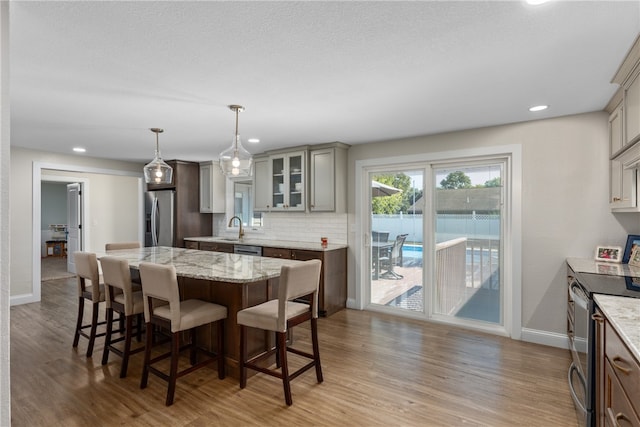 kitchen with stainless steel appliances, decorative light fixtures, light hardwood / wood-style flooring, gray cabinets, and a kitchen island