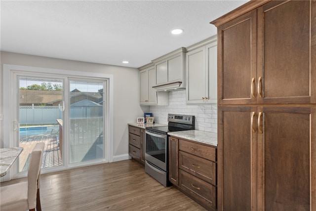 kitchen featuring light stone countertops, decorative backsplash, electric range, and light hardwood / wood-style floors