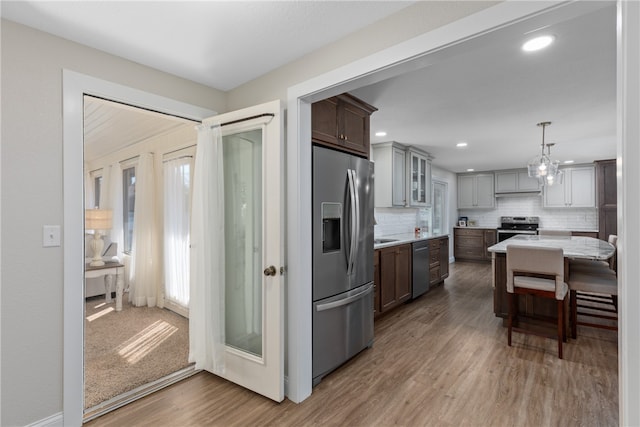 kitchen with hardwood / wood-style floors, gray cabinetry, appliances with stainless steel finishes, tasteful backsplash, and decorative light fixtures