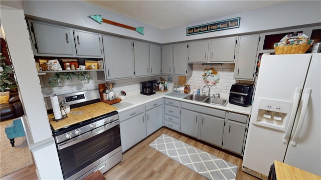 kitchen featuring sink, gray cabinetry, white refrigerator with ice dispenser, light hardwood / wood-style floors, and gas range