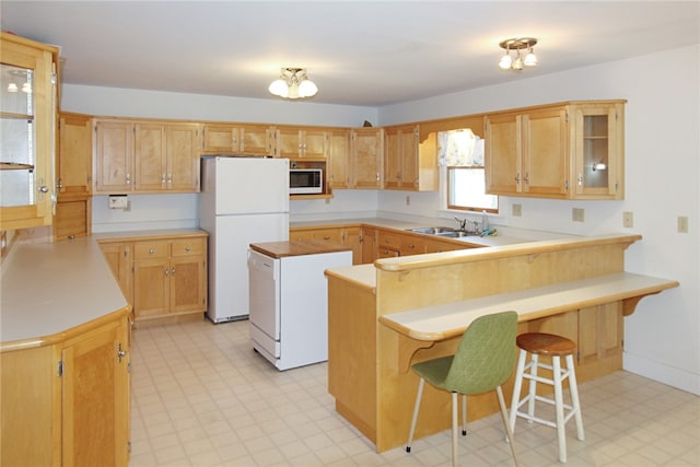 kitchen with kitchen peninsula, sink, white appliances, and a breakfast bar area