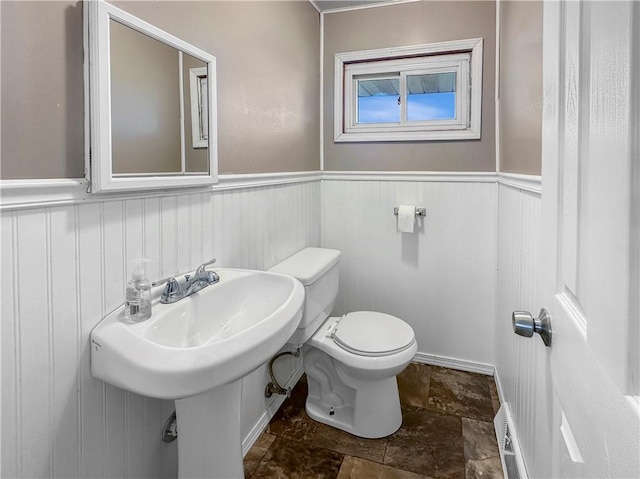 bathroom featuring toilet, stone finish flooring, and wainscoting