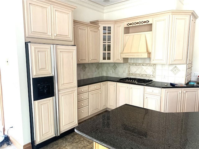 kitchen with premium range hood, stainless steel gas stovetop, dark stone counters, crown molding, and paneled refrigerator