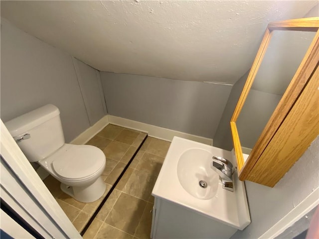 bathroom with toilet, vanity, a textured ceiling, tile patterned flooring, and baseboards