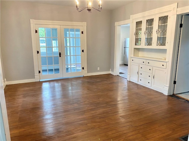 unfurnished dining area with baseboards, french doors, an inviting chandelier, and dark wood-style floors