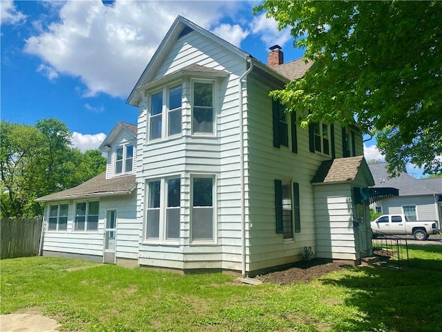 rear view of house with a yard, a chimney, a shingled roof, and fence