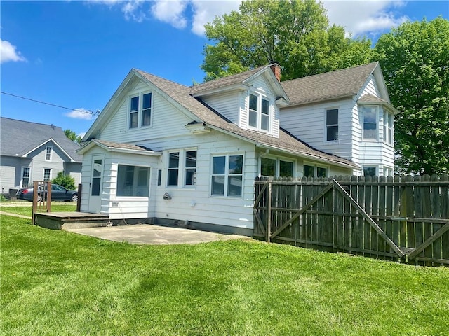 rear view of house featuring roof with shingles, fence, a yard, a patio, and a chimney