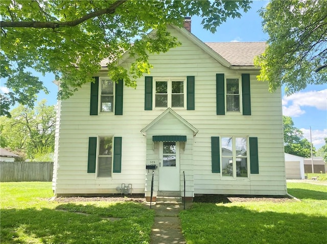 colonial house featuring a chimney, a front yard, a shingled roof, and fence
