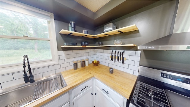 1006 Chicago Ave, Danville, IL 61832 - kitchen with butcher block countertops, wall chimney range hood, decorative backsplash, white cabinets, and a sink