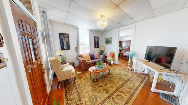 living area with a drop ceiling, wood finished floors, and an inviting chandelier