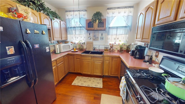 kitchen featuring wood-type flooring, light countertops, a sink, and black appliances