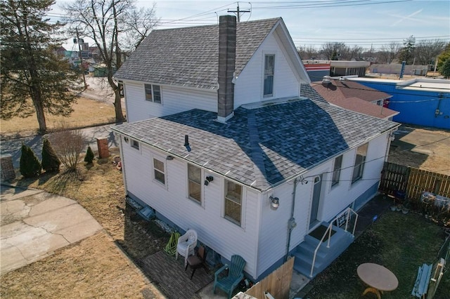 view of side of home with entry steps, a chimney, roof with shingles, fence, and a pool