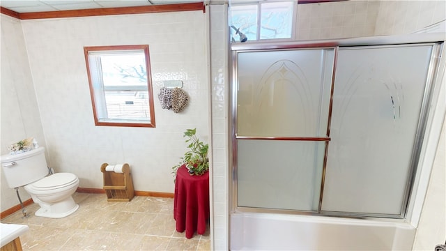 bathroom featuring tile patterned flooring, combined bath / shower with glass door, tile walls, and toilet