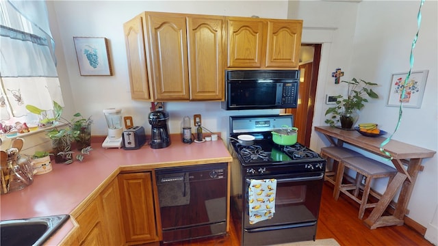 kitchen featuring a wealth of natural light, light countertops, black appliances, and wood finished floors