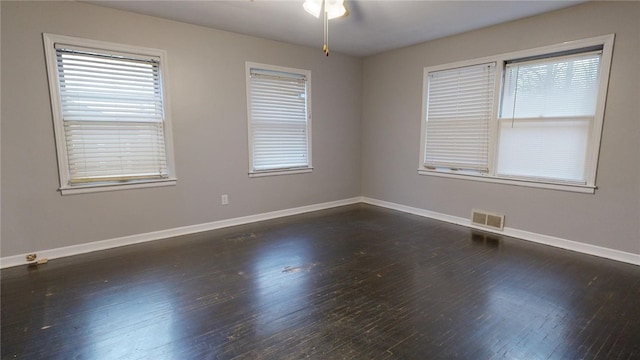 empty room with a healthy amount of sunlight, dark wood finished floors, visible vents, and baseboards