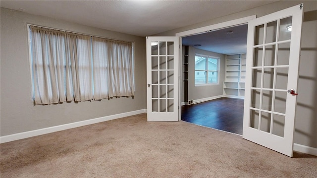 carpeted spare room featuring french doors and baseboards