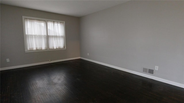 empty room featuring dark wood-style flooring, visible vents, and baseboards