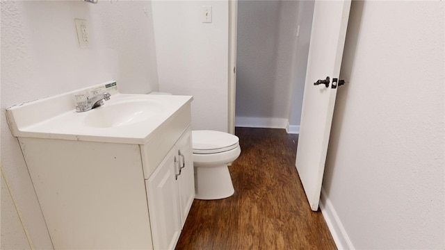 half bath with toilet, baseboards, wood finished floors, and vanity