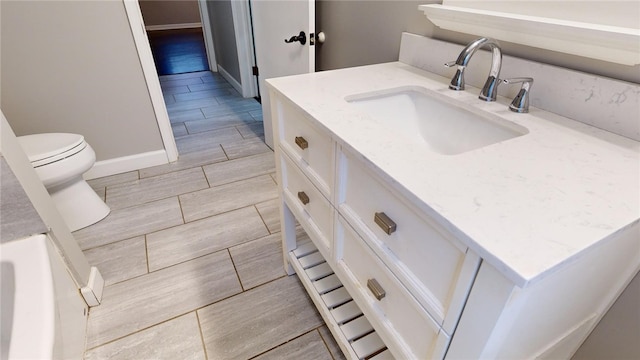 bathroom with wood finish floors, vanity, toilet, and baseboards