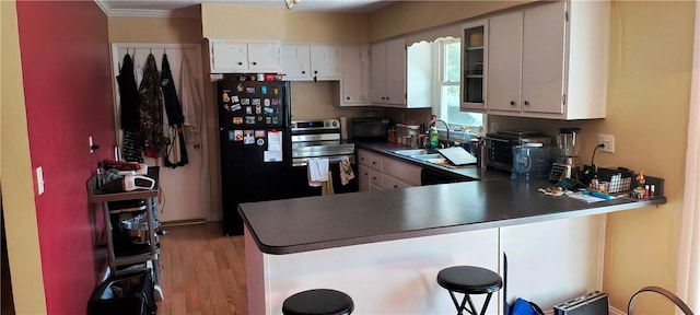 kitchen featuring white cabinetry, sink, black fridge, kitchen peninsula, and light wood-type flooring