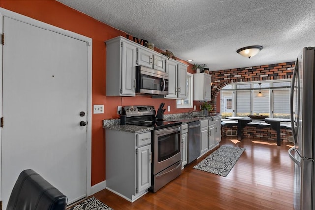 kitchen with dark wood-style floors, brick wall, and stainless steel appliances