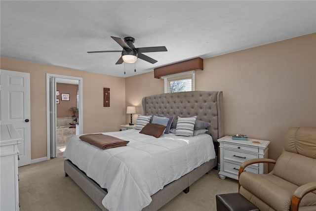 bedroom with a ceiling fan, light colored carpet, baseboards, and ensuite bathroom