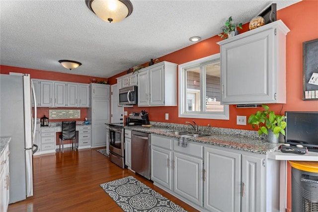 kitchen with stainless steel appliances, a sink, built in study area, light stone countertops, and dark wood finished floors