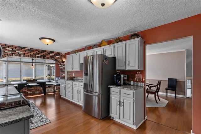 kitchen featuring baseboards, stainless steel fridge with ice dispenser, brick wall, dark wood-style flooring, and a textured ceiling