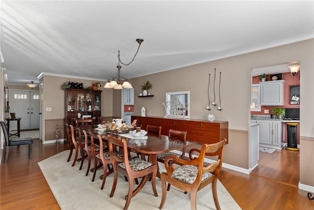 dining space featuring baseboards, crown molding, a chandelier, and wood finished floors